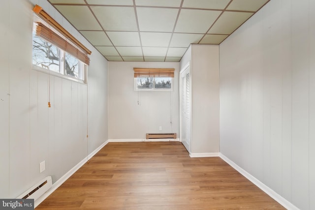 basement featuring a drop ceiling, a baseboard heating unit, and light hardwood / wood-style flooring