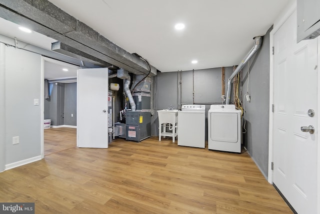 laundry room with light hardwood / wood-style floors, separate washer and dryer, heating unit, and sink