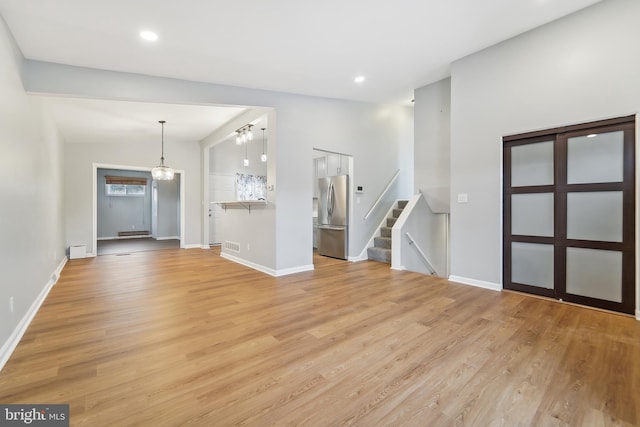 unfurnished living room featuring light hardwood / wood-style flooring, a notable chandelier, and lofted ceiling