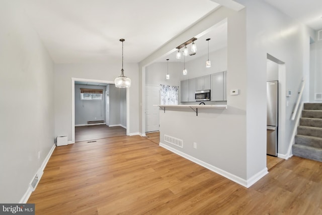 kitchen with a kitchen bar, stainless steel appliances, light hardwood / wood-style floors, hanging light fixtures, and high vaulted ceiling