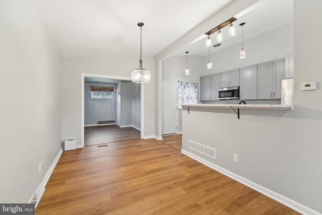 kitchen with refrigerator, a baseboard heating unit, gray cabinetry, kitchen peninsula, and a breakfast bar area