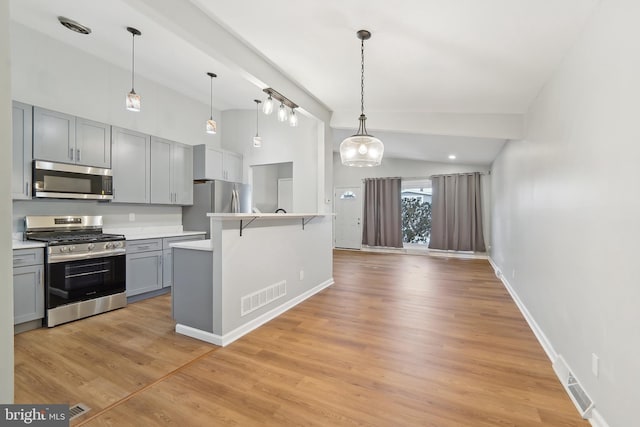 kitchen with pendant lighting, appliances with stainless steel finishes, lofted ceiling with beams, gray cabinets, and a breakfast bar area