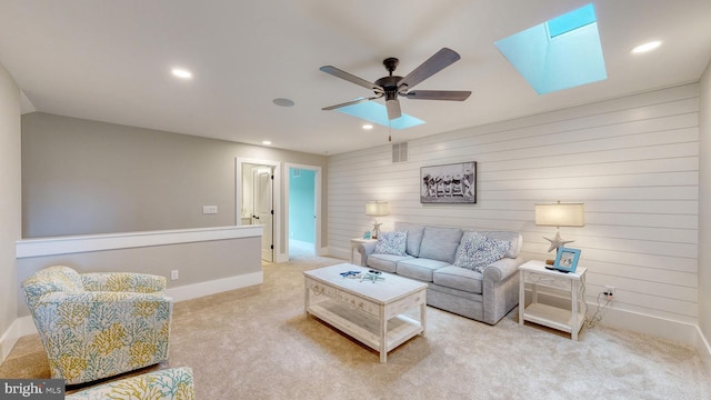 carpeted living room featuring ceiling fan, a skylight, and wood walls