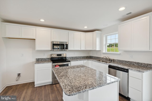 kitchen with light stone counters, a center island, white cabinets, and appliances with stainless steel finishes