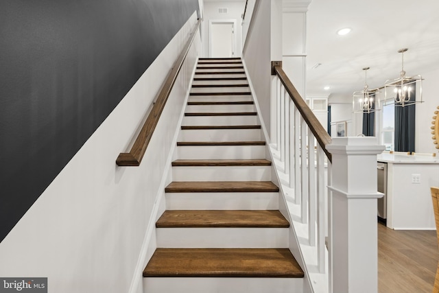 stairs featuring hardwood / wood-style floors and a chandelier