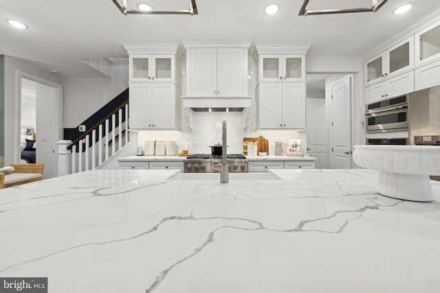 kitchen featuring white cabinets, stainless steel oven, and light stone countertops