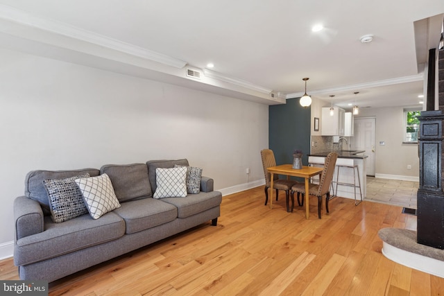 living room featuring sink, light hardwood / wood-style floors, a wood stove, and crown molding