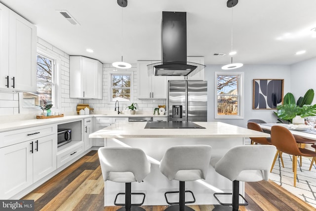 kitchen with hanging light fixtures, island range hood, white cabinets, and stainless steel appliances