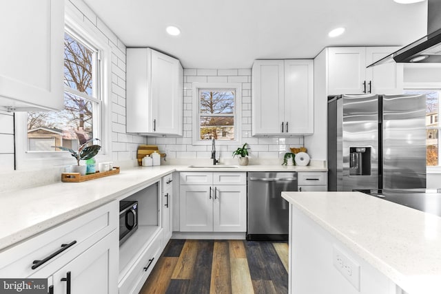 kitchen with appliances with stainless steel finishes, tasteful backsplash, sink, white cabinets, and exhaust hood