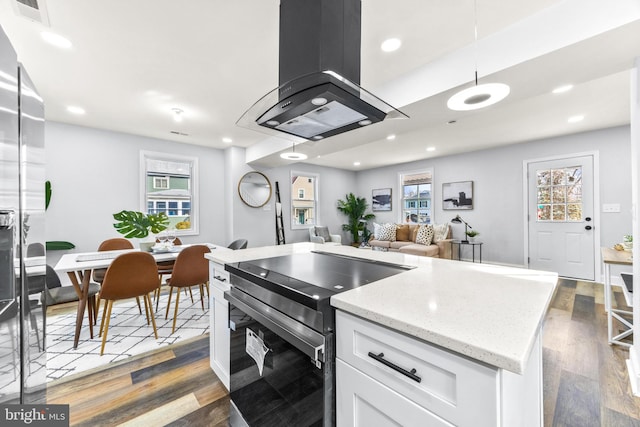 kitchen with dark wood-type flooring, stainless steel range with electric stovetop, island range hood, white cabinets, and decorative light fixtures