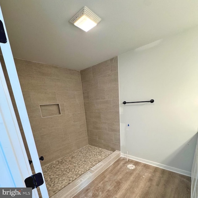 full bath featuring tiled shower, wood finished floors, and baseboards