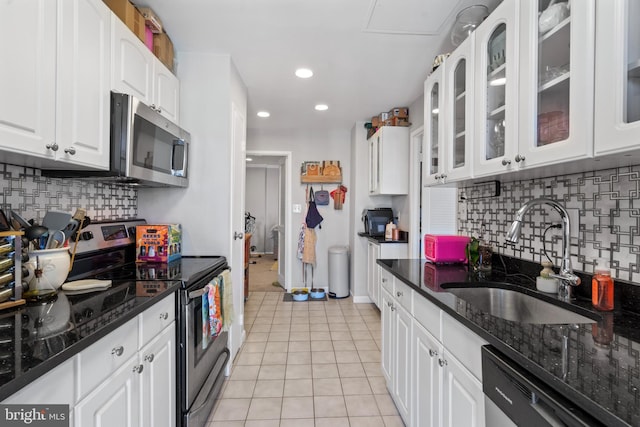 kitchen with sink, light tile patterned floors, appliances with stainless steel finishes, dark stone countertops, and white cabinets