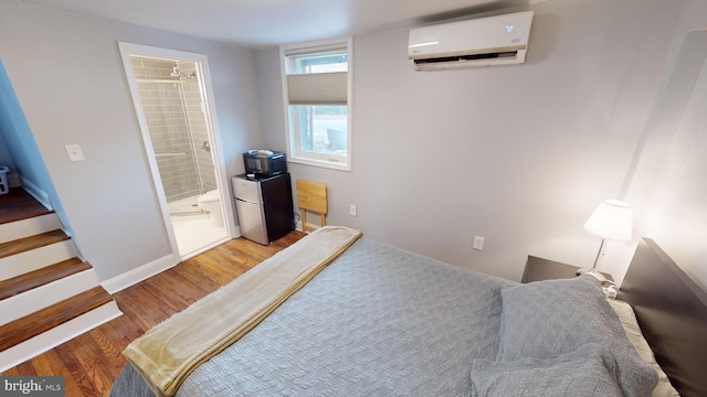 bedroom with wood-type flooring, ensuite bathroom, and a wall unit AC