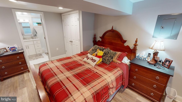 bedroom featuring a closet, ensuite bathroom, electric panel, and light hardwood / wood-style flooring