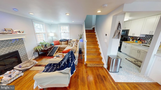 living room with a tile fireplace, ornamental molding, and light hardwood / wood-style flooring