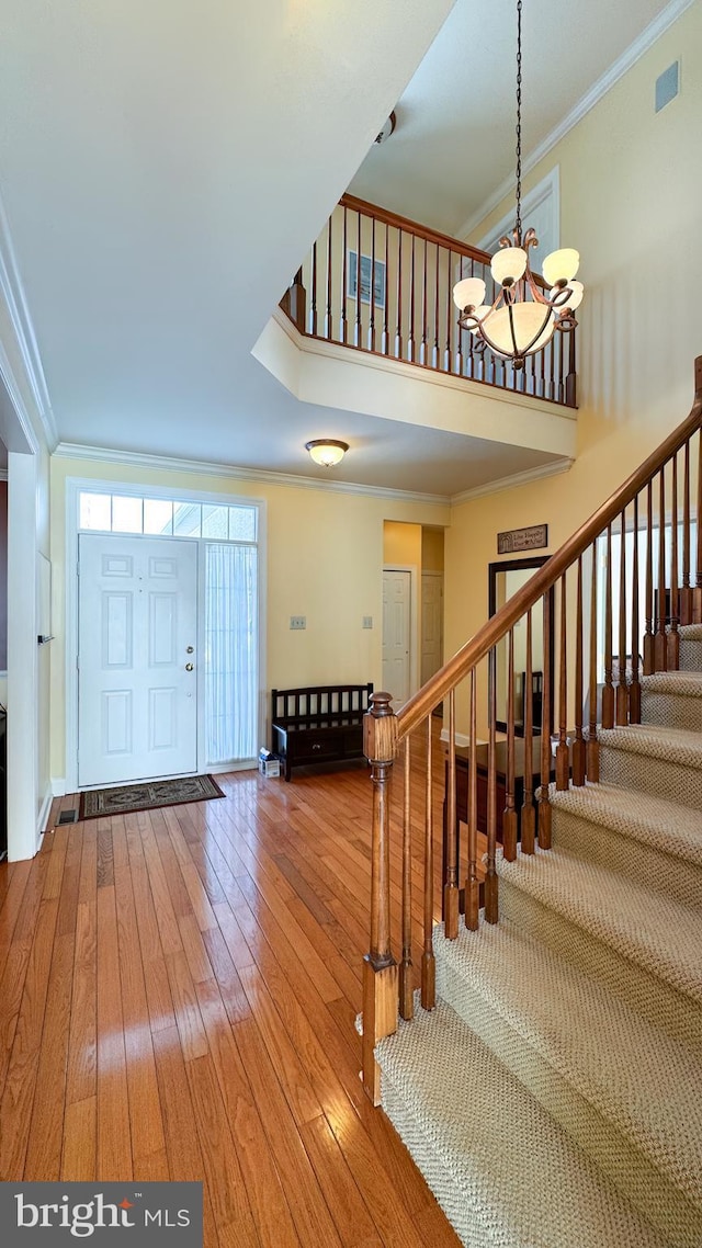 entryway with hardwood / wood-style flooring, crown molding, and a notable chandelier