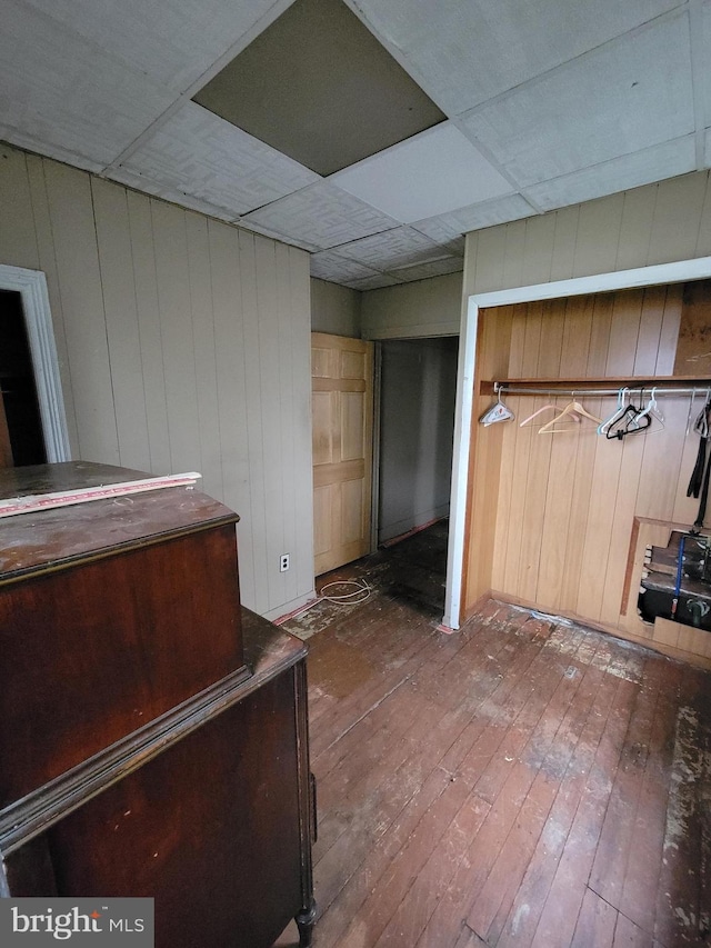 interior space with a paneled ceiling, hardwood / wood-style floors, wood walls, and a closet