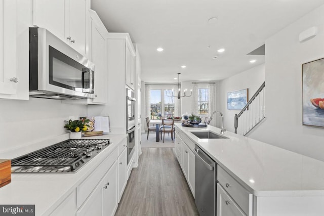 kitchen with white cabinets, decorative light fixtures, stainless steel appliances, sink, and a center island with sink