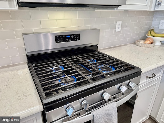 details featuring stainless steel gas range, white cabinetry, light stone counters, and decorative backsplash