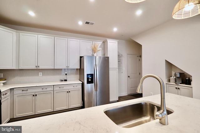 kitchen with stainless steel fridge, light stone counters, white cabinets, and a sink