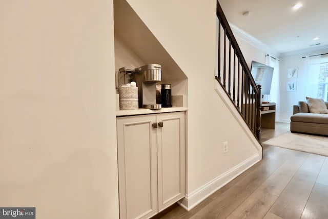 bar with ornamental molding, stairway, light wood-style flooring, and baseboards