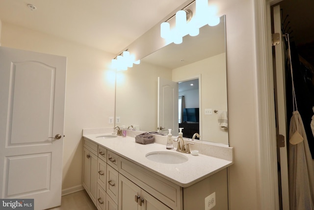 bathroom featuring double vanity, connected bathroom, baseboards, and a sink