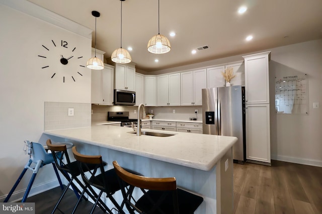 kitchen featuring a peninsula, a sink, white cabinets, hanging light fixtures, and appliances with stainless steel finishes