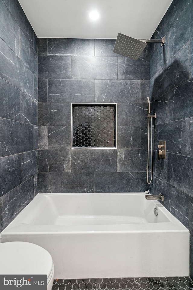 bathroom featuring toilet, tiled shower / bath, and tile walls