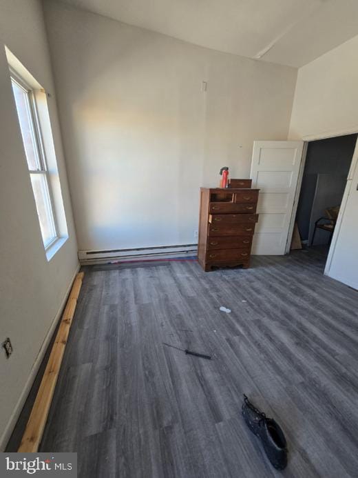 unfurnished bedroom featuring a baseboard heating unit and dark hardwood / wood-style floors