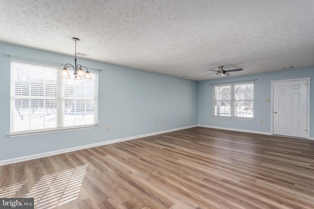 empty room featuring hardwood / wood-style flooring, a wealth of natural light, a textured ceiling, and ceiling fan with notable chandelier