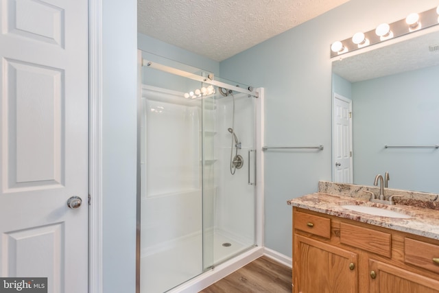 bathroom featuring wood-type flooring, a textured ceiling, a shower with shower door, and vanity