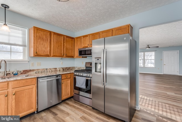 kitchen with light stone countertops, a textured ceiling, stainless steel appliances, sink, and hanging light fixtures