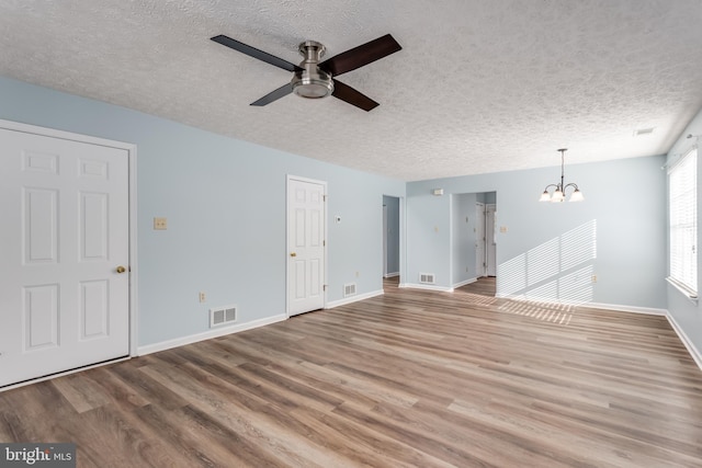 unfurnished living room featuring ceiling fan with notable chandelier, hardwood / wood-style floors, and a textured ceiling