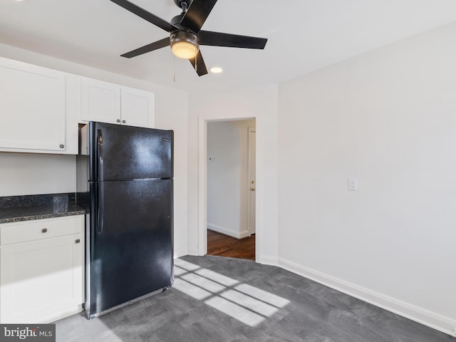 kitchen featuring white cabinets, dark stone countertops, black fridge, dark wood-type flooring, and ceiling fan