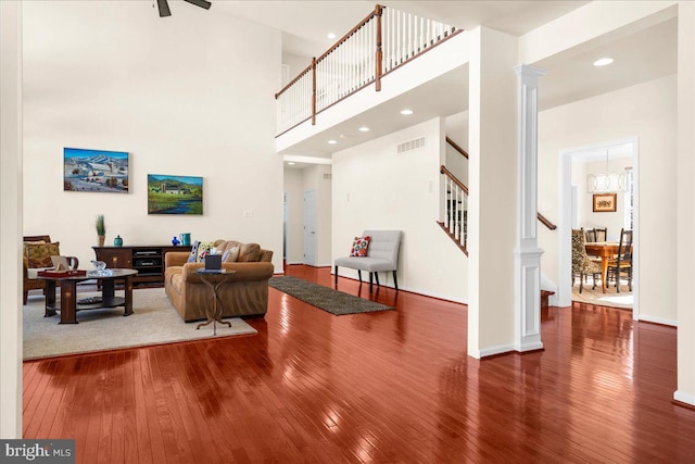 living room featuring a towering ceiling, decorative columns, and hardwood / wood-style flooring