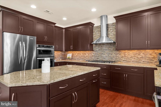 kitchen featuring tasteful backsplash, appliances with stainless steel finishes, wall chimney exhaust hood, and light stone countertops