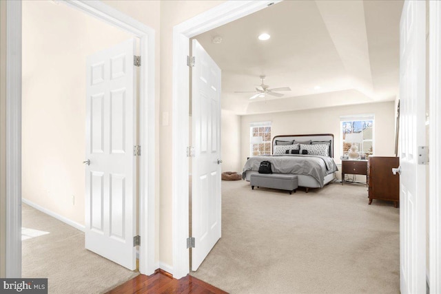 bedroom featuring a raised ceiling, light colored carpet, and ceiling fan