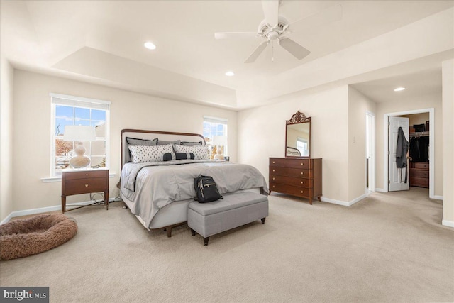 bedroom featuring a raised ceiling, light colored carpet, ceiling fan, and multiple windows