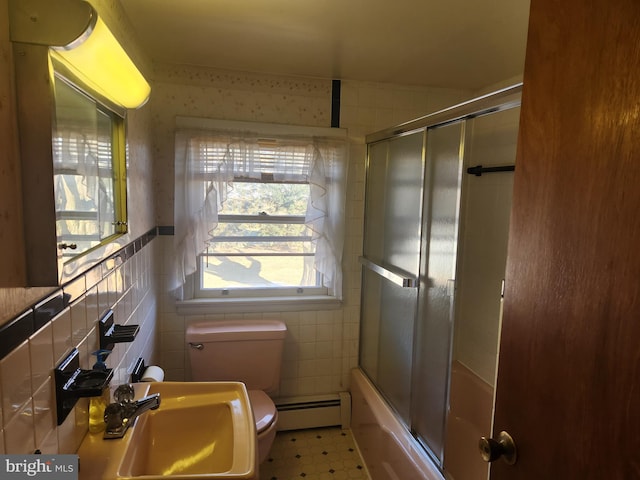 full bathroom featuring baseboard heating, tile walls, sink, combined bath / shower with glass door, and toilet