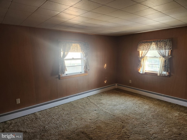 empty room featuring plenty of natural light, a baseboard heating unit, wooden walls, and carpet flooring