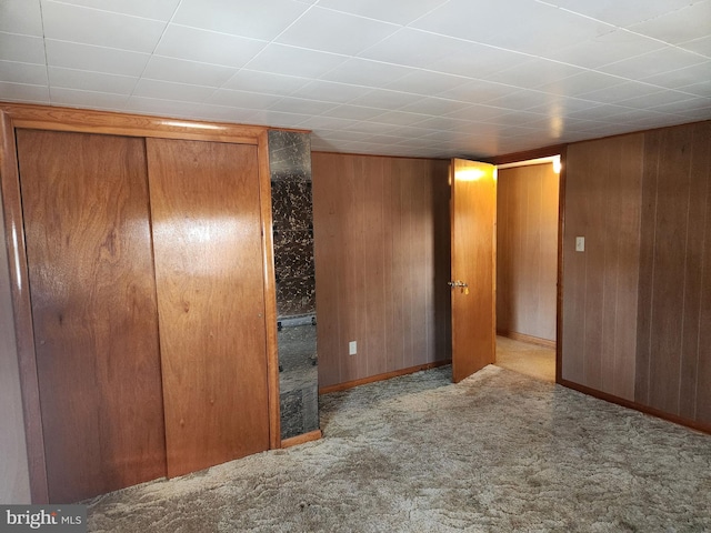 unfurnished bedroom featuring a closet, wooden walls, and light carpet