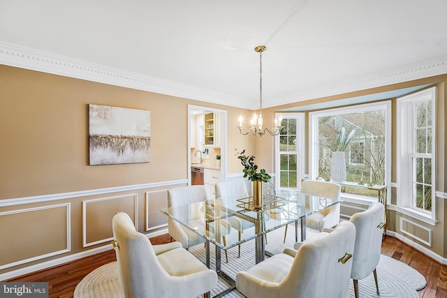 dining room with wainscoting, wood finished floors, crown molding, a decorative wall, and a notable chandelier