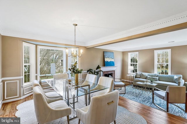 dining room with crown molding, light wood finished floors, a fireplace, and a notable chandelier