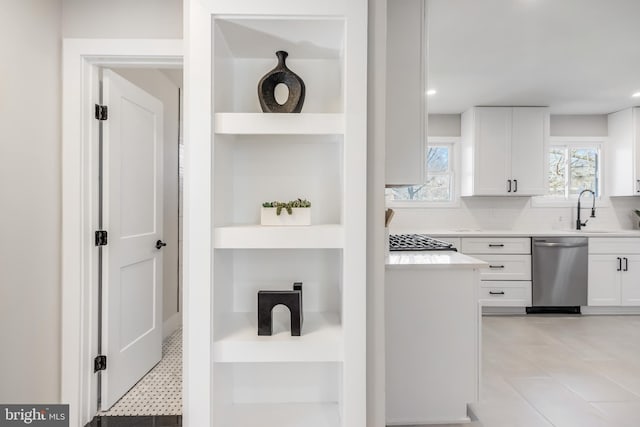 kitchen with built in shelves, a sink, white cabinets, light countertops, and dishwasher