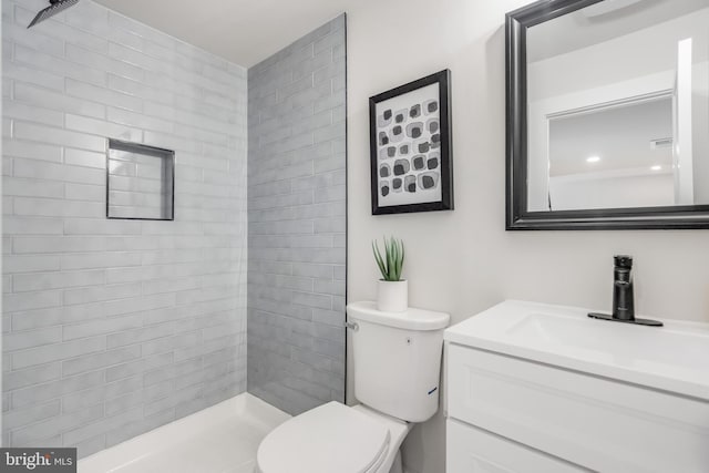 bathroom with a tile shower, vanity, and toilet