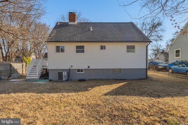 back of house featuring a shingled roof, a lawn, a chimney, stairs, and cooling unit