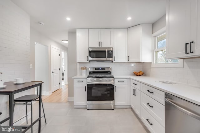 kitchen with stainless steel appliances, tasteful backsplash, light countertops, and white cabinets