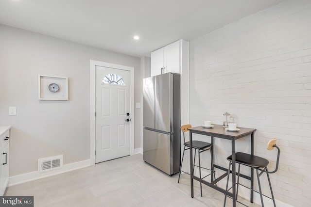 kitchen featuring visible vents, brick wall, freestanding refrigerator, and white cabinetry