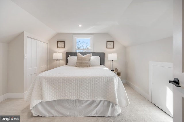 bedroom featuring vaulted ceiling, a closet, light carpet, and baseboards