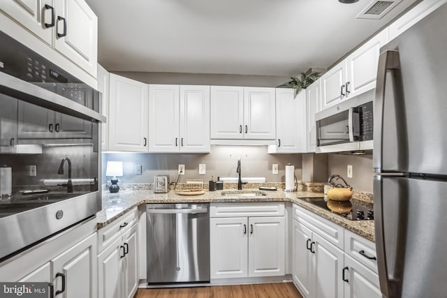 kitchen with white cabinetry, sink, stainless steel appliances, light stone countertops, and light wood-type flooring